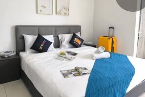 Een net opgemaakt bed met kussens, een blauwe deken, een tijdschrift en een gele koffer.