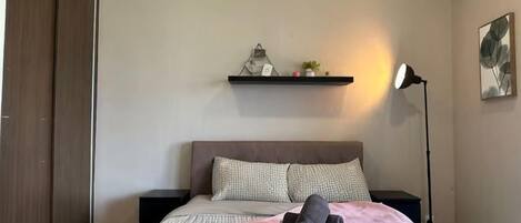 A bedroom with a bed, bedside tables, a wardrobe, a shelf with decorative items, and a floor lamp.