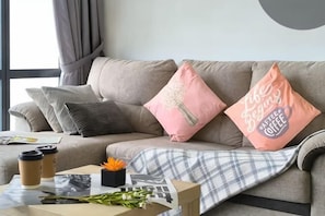 En stue med sofa, puder, et sofabord med et magasin og et vindue med gardiner.