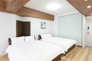 A bedroom with two beds, wooden ceiling beams, a white wall, and a door. - Excellence Osakajo Koen (Osaka)