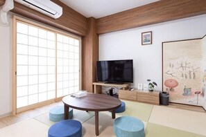 Una habitación con suelo de tatami, techo de madera, televisor, un cuadro y una puerta corrediza.