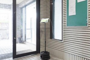 A room with a tiled floor, a door leading outside, a bulletin board, and a tire on the floor. - Excellence Osakajo Koen (Osaka)