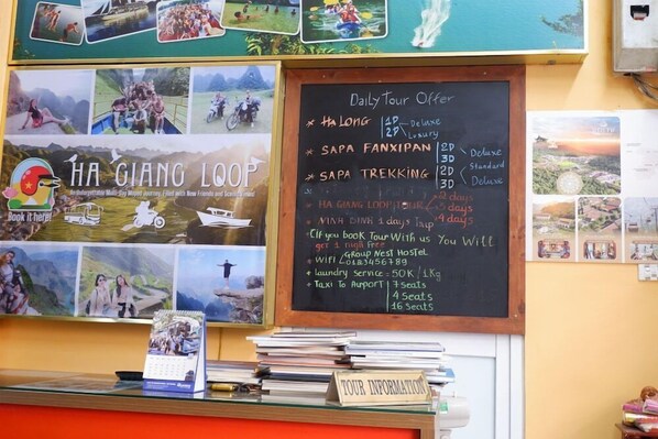 Mostrador de agencia de viajes con una pizarra que enumera opciones de tour, un calendario y un cartel que dice 'Reserva aquí'.