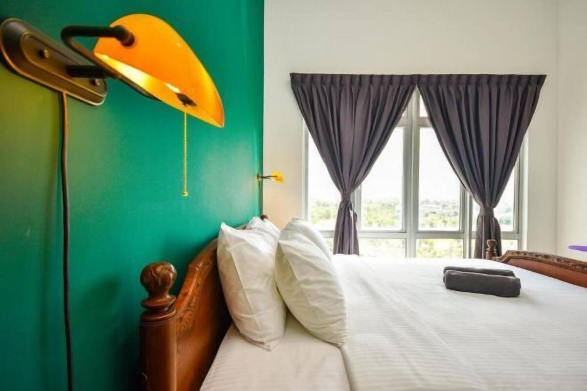 Una habitación de hotel con cama, mesita de noche, lámpara y ventana con cortinas.