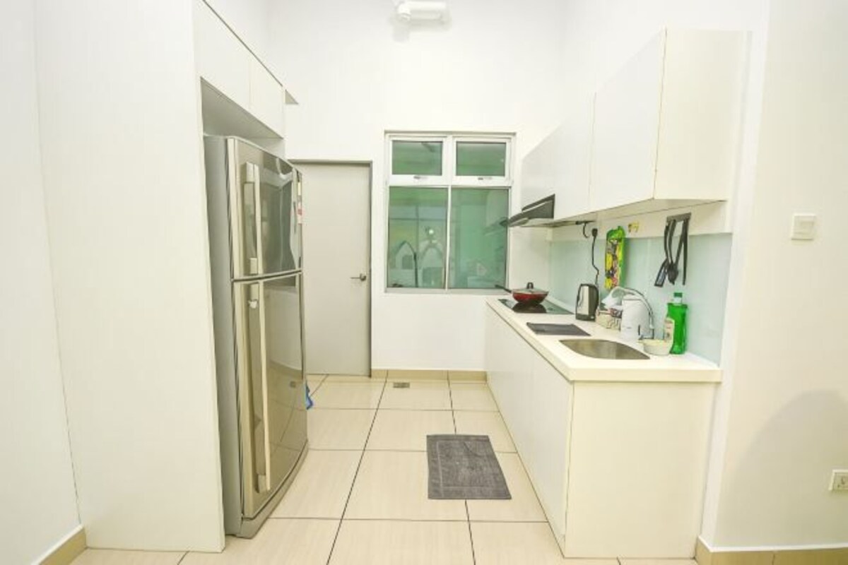 Cocina compacta con gabinetes blancos, un refrigerador de acero inoxidable, una ventana y una pequeña encimera con un lavamanos y diversos objetos.