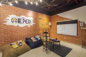 Una habitación con pared de ladrillo, una pizarra, un sofá con cojines y una pantalla para proyector.