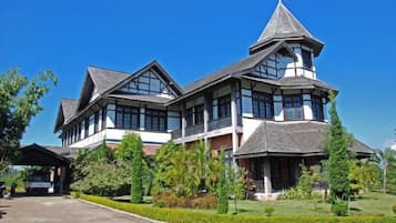A large, two-story building with a prominent tower, surrounded by well-maintained gardens and a clear sky.