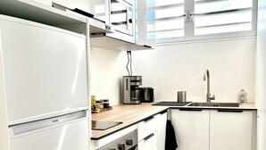 Une cuisine compacte avec des meubles blancs, un four à micro-ondes encastré, une machine à café et un évier.