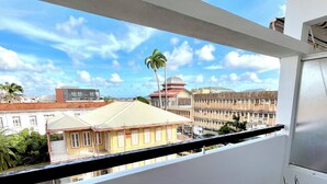 Un balcon offrant une vue dégagée sur le paysage urbain, avec des bâtiments et un palmier.