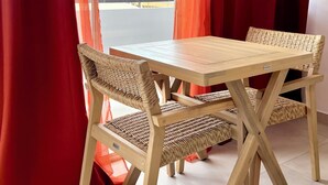 Une pièce avec une table en bois et des chaises en osier, des rideaux rouges et une vue sur un bâtiment doté d’un dôme et bordé de palmiers.
