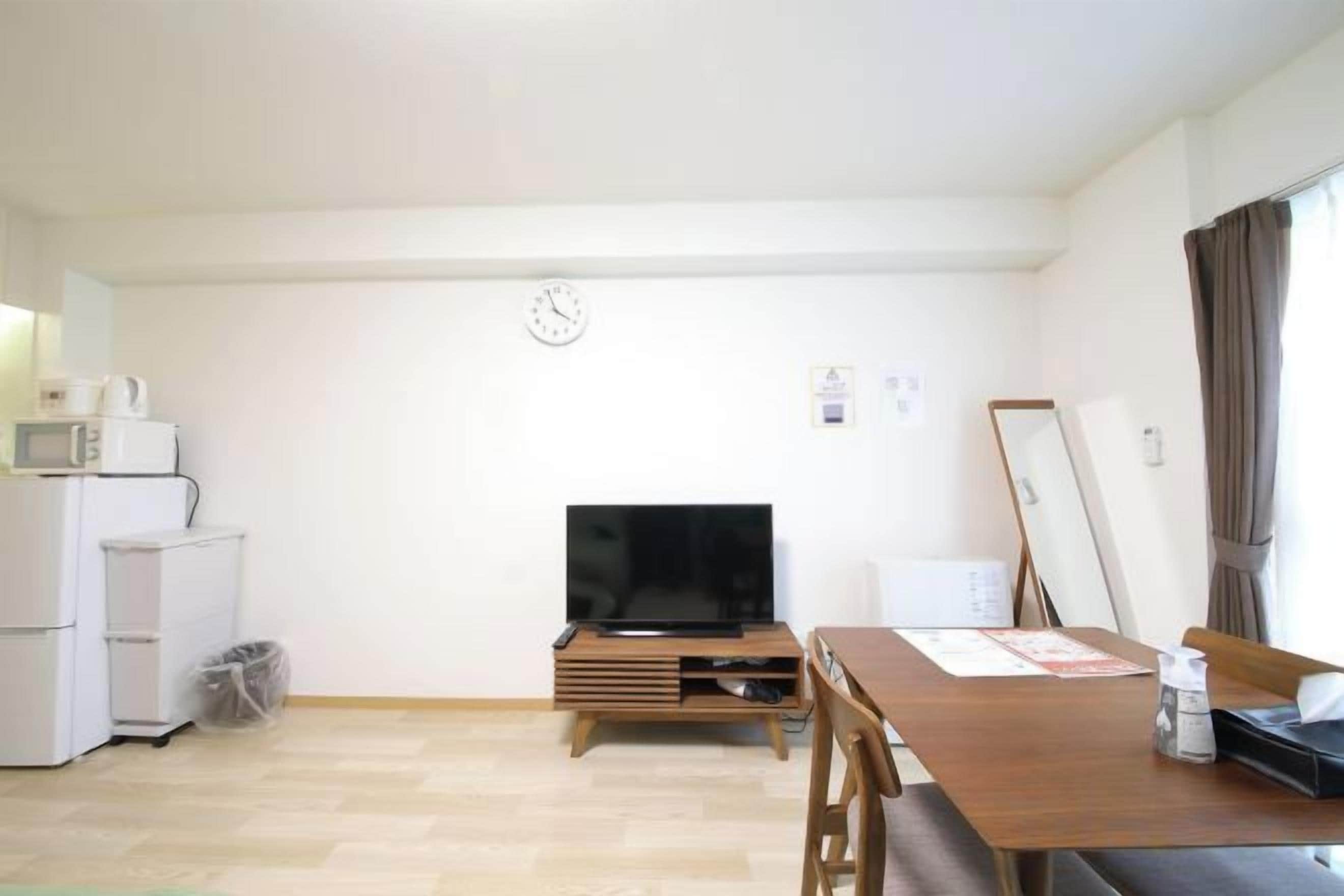 A compact living space with a kitchenette, a flat-screen TV, a dining table, and a window with curtains.
