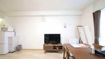 A compact living space with a kitchenette, a flat-screen TV, a dining table, and a window with curtains.
