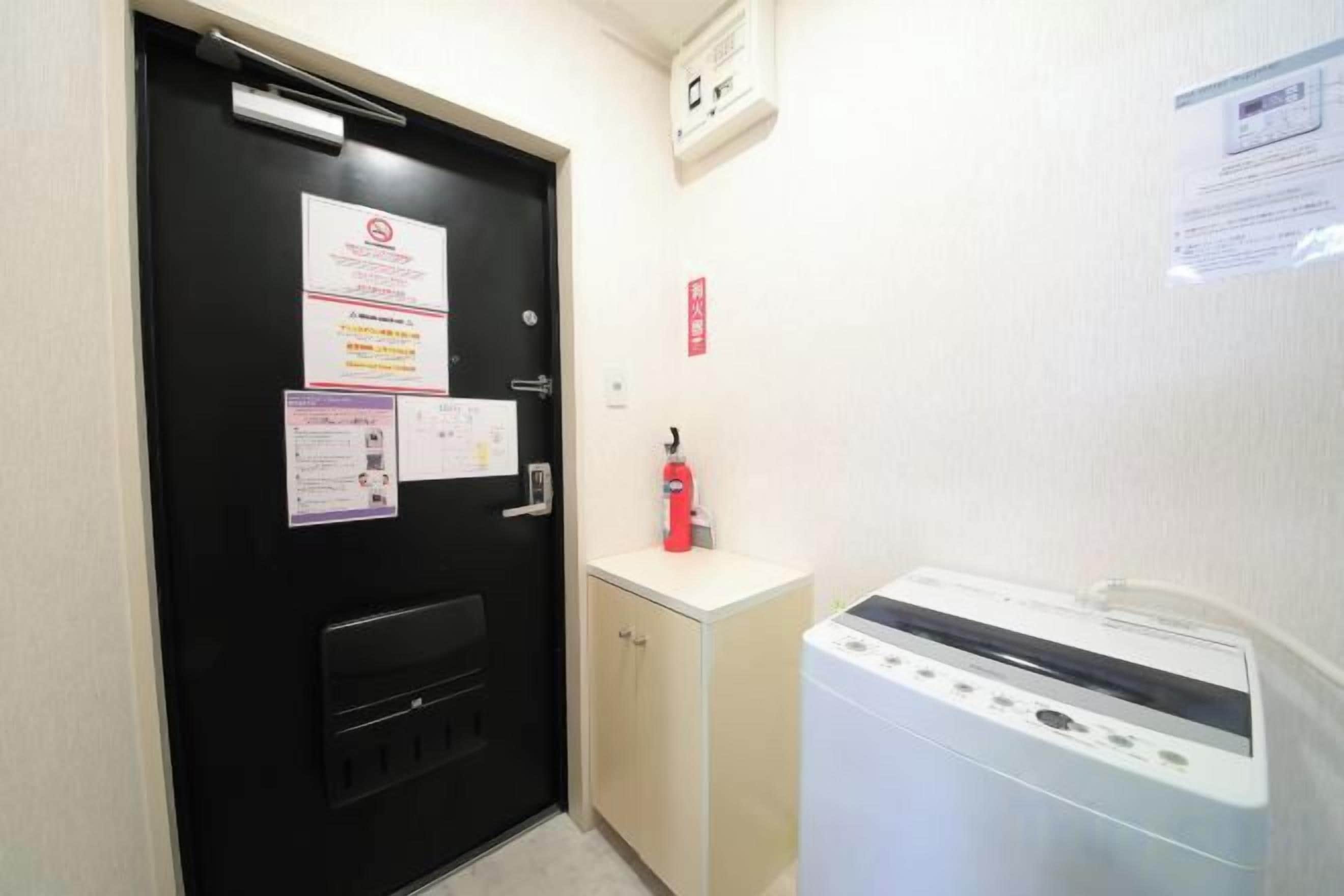 Une chambre d’hôtel avec une porte noire, un lave-linge blanc, un extincteur et un avis affiché sur le mur.