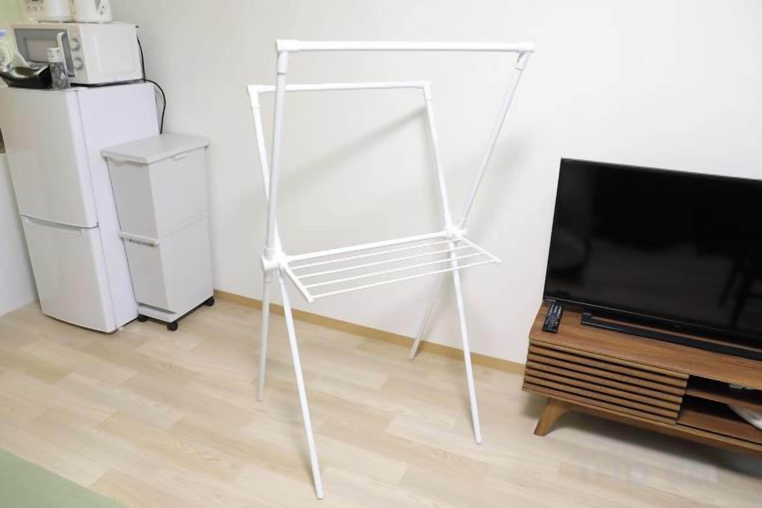 A room with a white metal drying rack, a white refrigerator, and a wooden entertainment unit with a flat-screen TV.