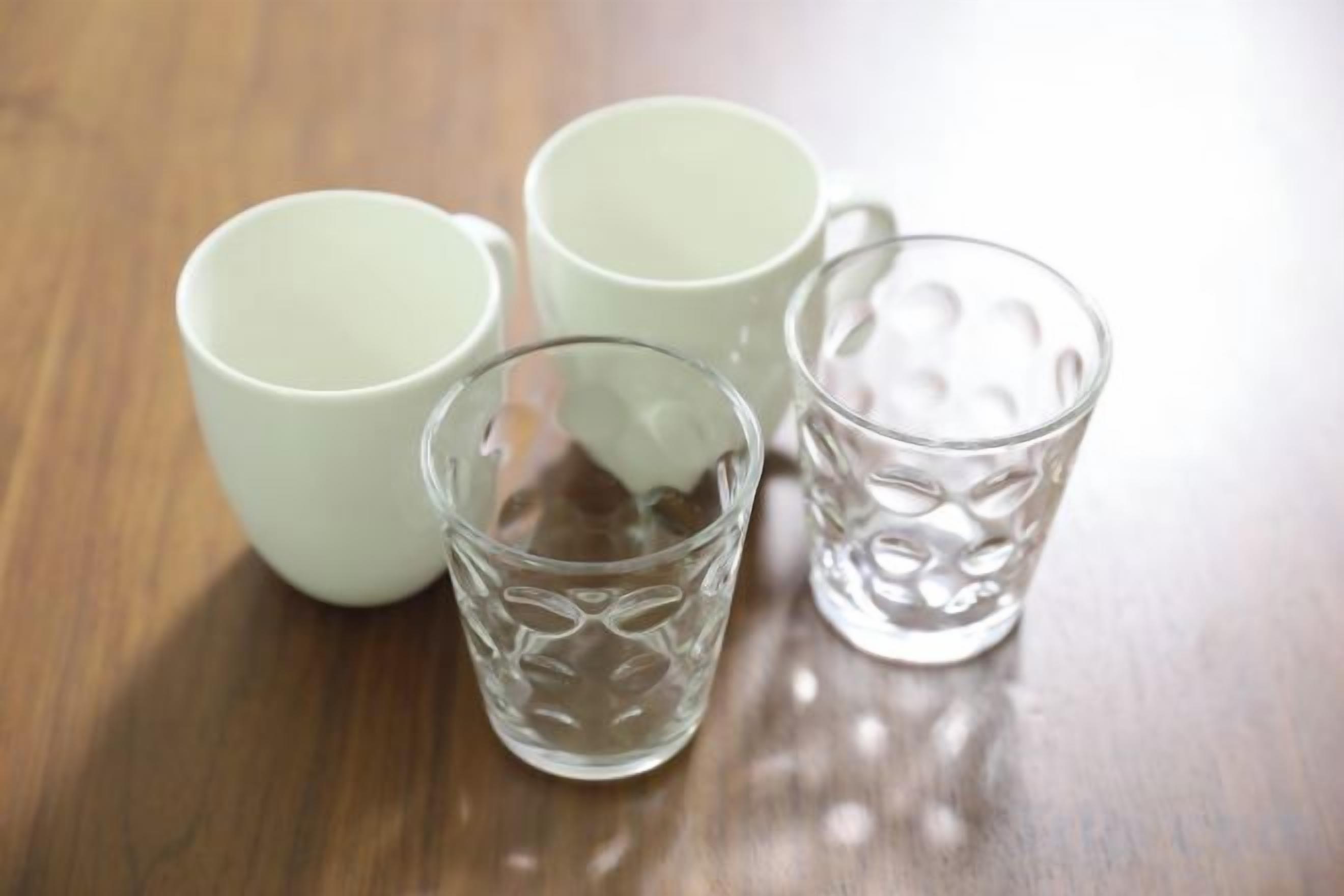 Tres tazas de cerámica blanca y una taza de vidrio transparente sobre una superficie de madera.