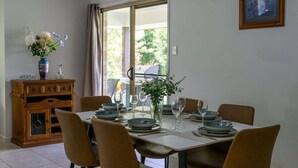Un comedor con una mesa dispuesta para cuatro personas, un aparador de madera y un jarrón con flores.