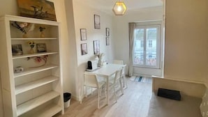 A room with a white desk, chairs, a bookshelf, framed pictures on the wall, and a window with a view of buildings. - Charming Studio in the 7th District of Paris (Paris)