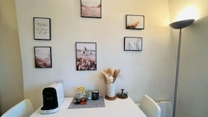 A dining area with a white table, framed artwork on the wall, a coffee machine, and a vase with dried plants. - Charming Studio in the 7th District of Paris (Paris)