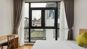 Un dormitori amb una finestra gran, un llit, una cadira i vista cap a edificis.