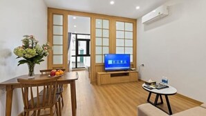 Un saló modern amb una taula de dinar de fusta, un televisor sobre un moble de fusta, una taula rodona petita amb una cadira i un ram de flors.