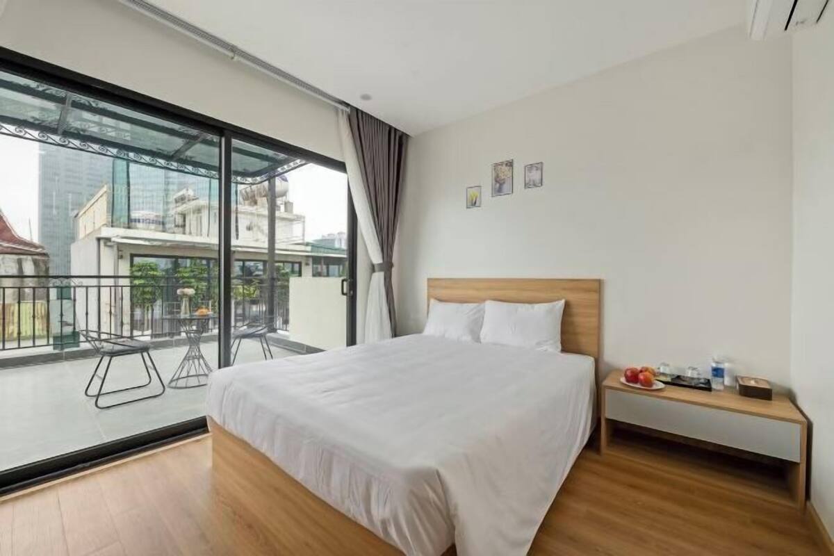 Una habitación de hotel con una cama grande, una mesita de noche de madera y un balcón con barandilla de vidrio.