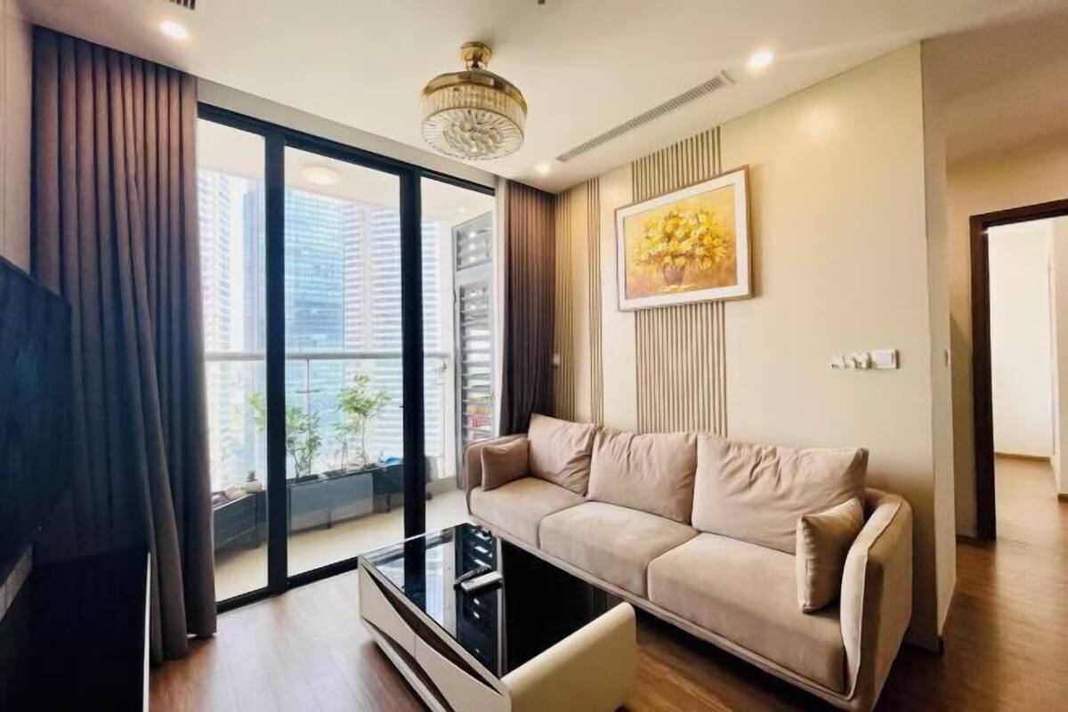 Uma sala de estar moderna com um sofá, uma mesa de centro de vidro e uma grande janela com vista para edifícios.