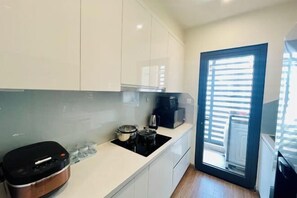 A modern kitchen with white cabinets, a black stove, a coffee maker, and a sliding glass door leading to a balcony.