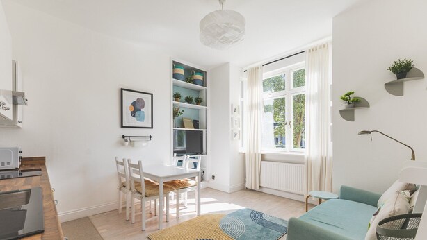A modern, well-lit room with a dining table, chairs, a sofa, and a bookshelf. - Stylish West London Stay by Hammersmith (London)