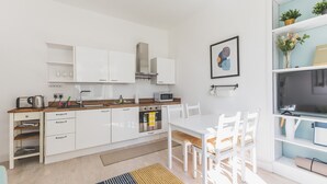 A modern kitchen with white cabinets, a wooden countertop, and a dining area with white chairs. - Stylish West London Stay by Hammersmith (London)