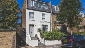 A two-story residential building with a white facade, a dark roof, and a brick chimney. - Stylish West London Stay by Hammersmith (London)