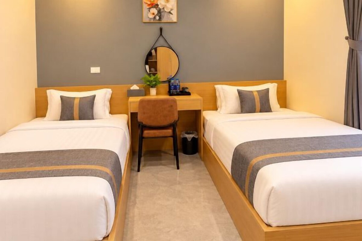 A hotel room with two single beds, a desk with a chair, a mirror, and a small table with a plant.