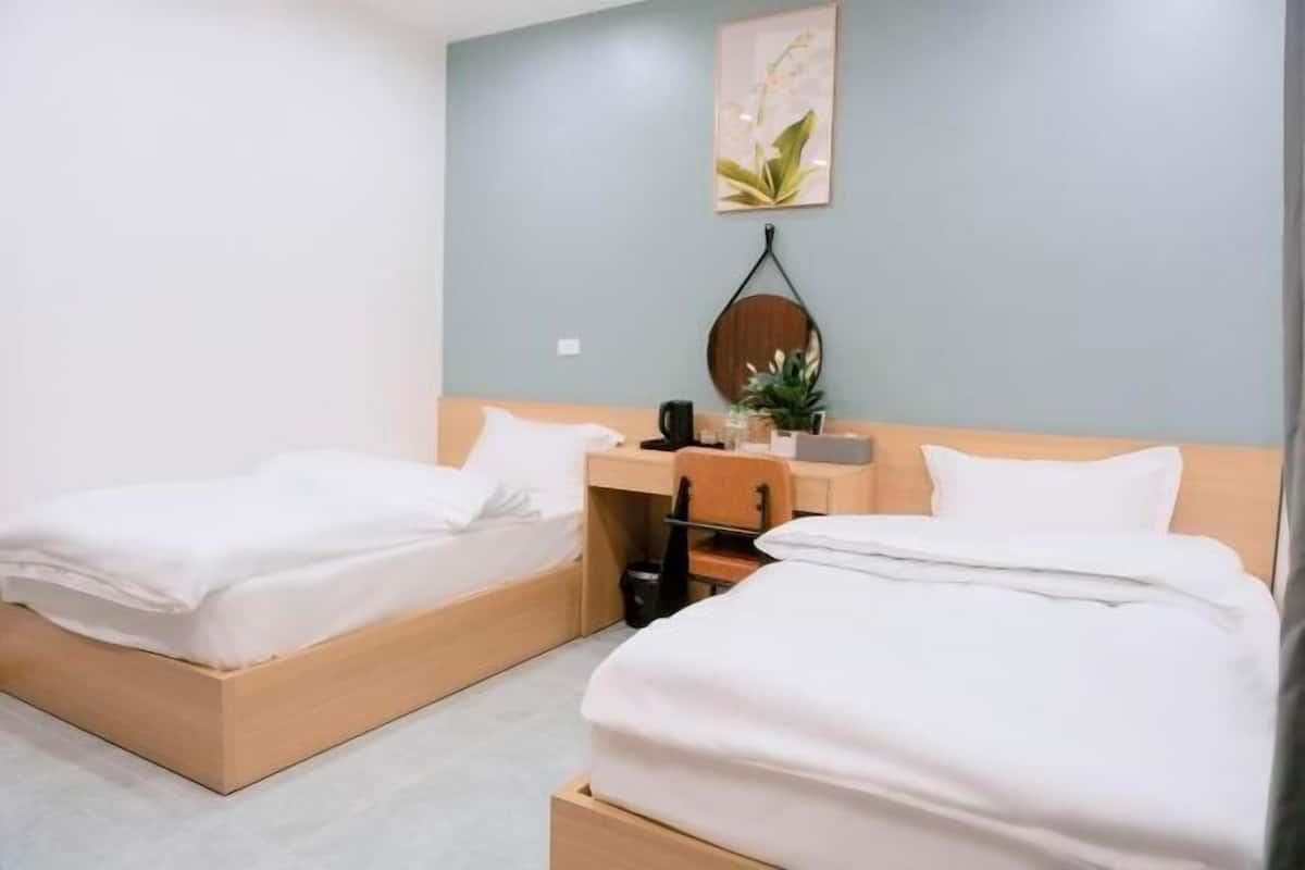 Une chambre d’hôtel avec deux lits simples, un bureau avec une chaise, une petite table, une plante en pot et un miroir rond fixé au mur.