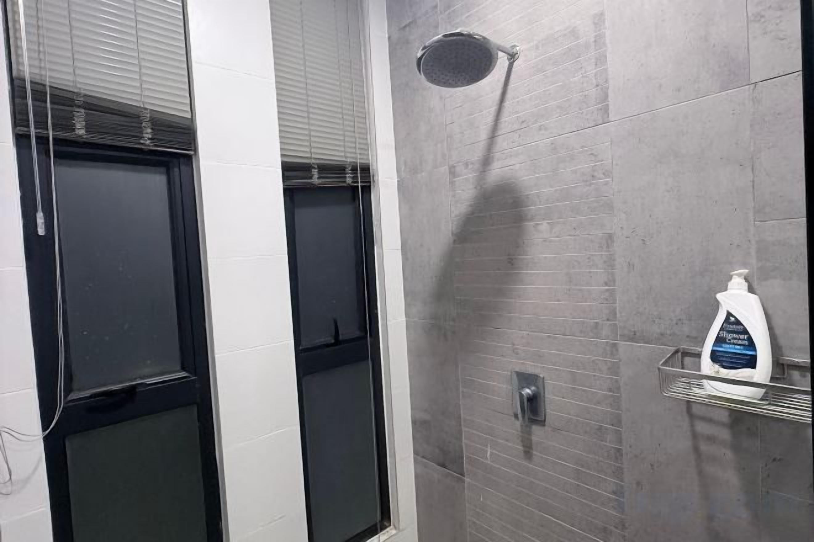 A bathroom with a shower, a glass door, and a soap dispenser on a shelf.