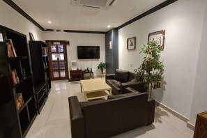 Una sala de estar con sofá, televisor, estantería y una planta en maceta.