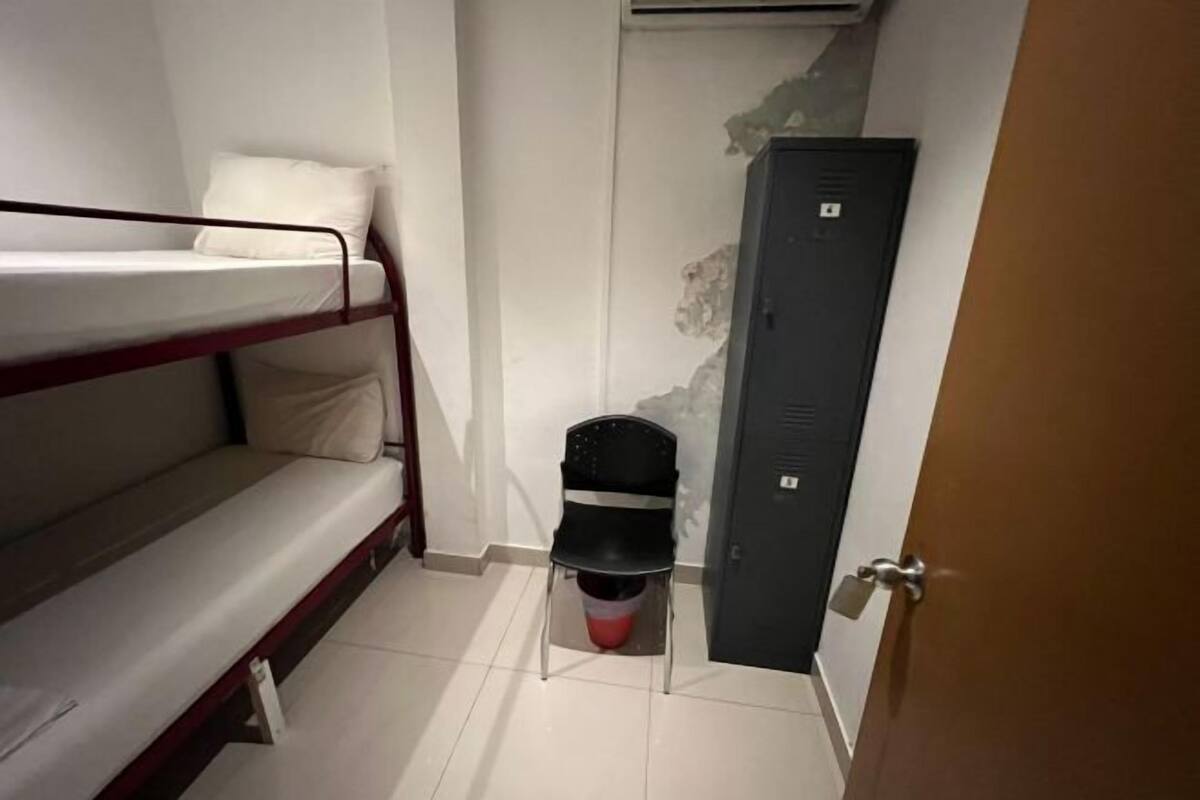 Une petite pièce compacte, équipée d’un lit superposé, d’une chaise, d’une porte et d’un casier fixé au mur.