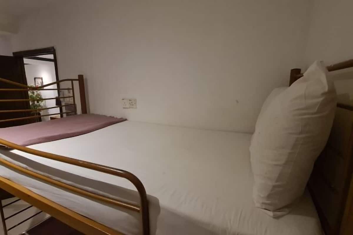 Un lit simple avec un cadre en bois et un matelas blanc, un oreiller blanc et une petite table de chevet avec une lampe.