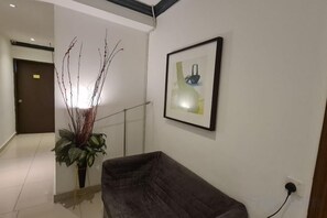 Un pasillo con un sofá de color oscuro, una planta en maceta y un cuadro en la pared.