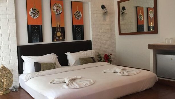 Habitación de hotel con cama, almohadas, mesita de noche, espejo y obras de arte en la pared.
