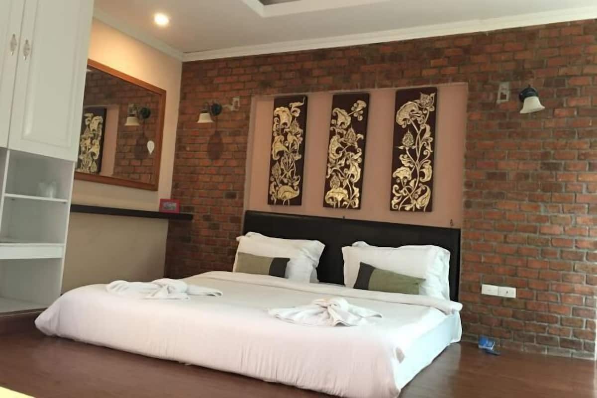 A hotel room with a brick wall, a bed with white bedding, a headboard, and a wall-mounted light fixture.