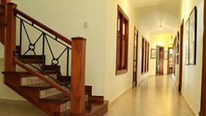 Una escalera de madera con barandilla de vidrio, un pasillo con cuadros enmarcados y una puerta al final.