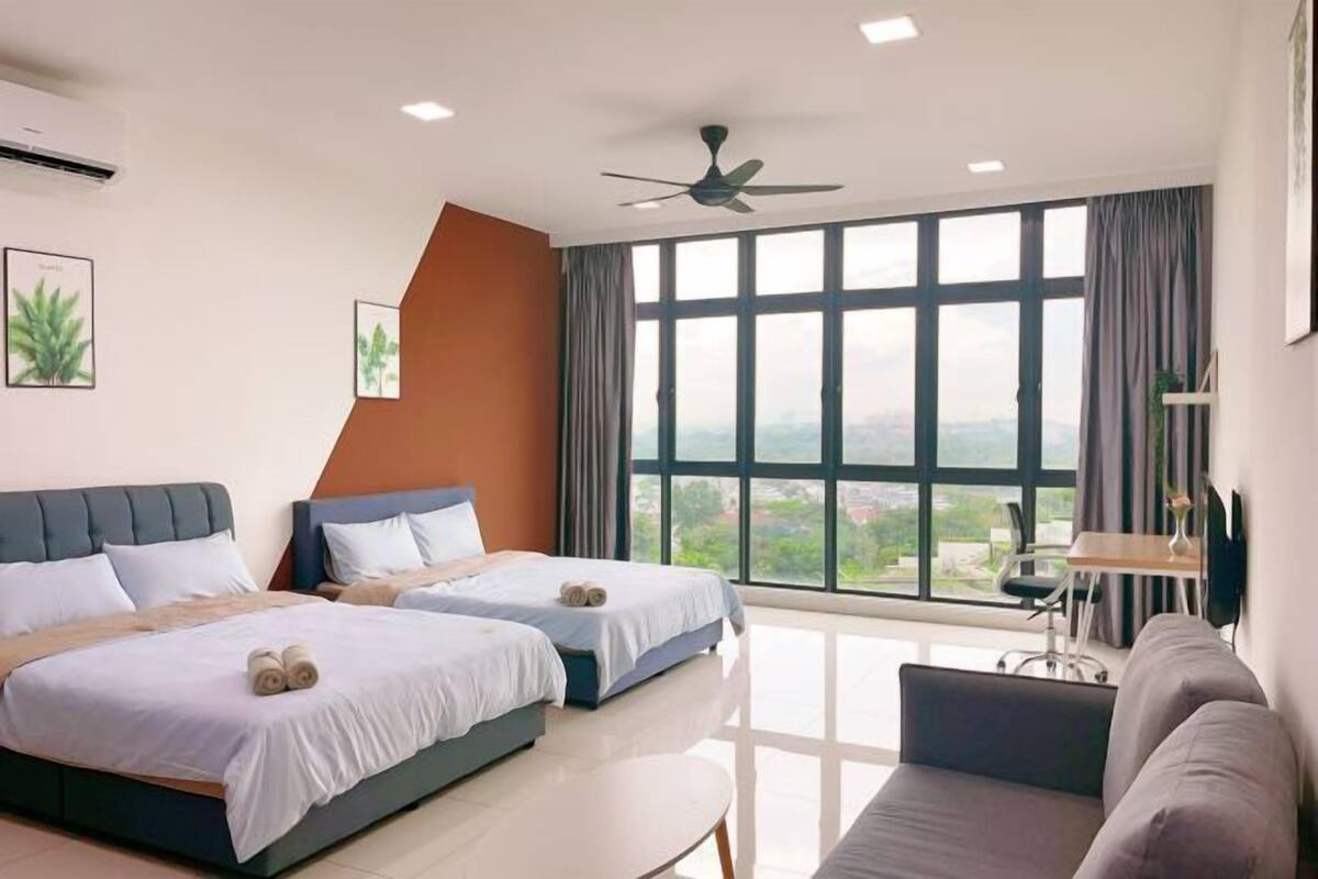 A hotel room with two beds, a sofa, a desk, a ceiling fan, and large windows with a view.