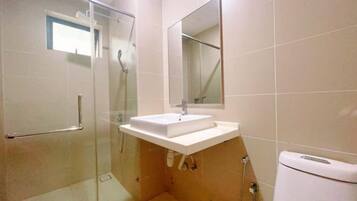 Un baño moderno con cabina de ducha de vidrio, un lavamanos blanco y un espejo sobre él.