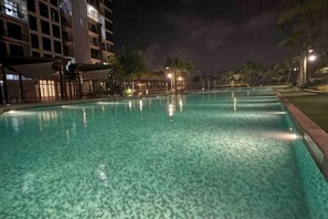 Una piscina con agua cristalina, rodeada de palmeras y un edificio de varios pisos.