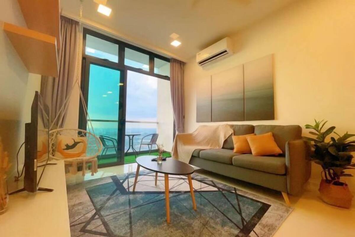 A modern living room with a sofa, a coffee table, and a TV. There is a balcony with a view.