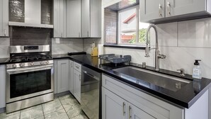 A modern kitchen with stainless steel appliances, white cabinetry, and a black countertop. - Modern 3BR Bay Stay: pet/family-friendly, yard, parking, W/D, near hospitals (MORENO VALLEY)