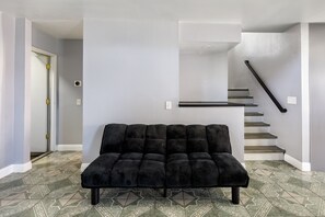 Un sofà negre en una habitació amb rajoles de terra estampades, una escala i una porta.
