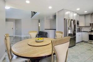 A modern kitchen with stainless steel appliances, a dining area with a round table and chairs, and a staircase leading to an upper level.