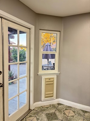 A corner room with a door, a window with a view of outdoor furniture, and patterned floor tiles.