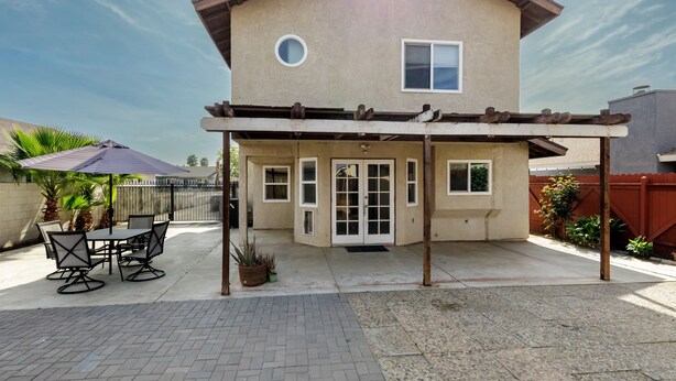 A two-story house with a covered patio area, a dining table with chairs, and a potted plant. - Modern 3BR Bay Stay: pet/family-friendly, yard, parking, W/D, near hospitals (MORENO VALLEY)