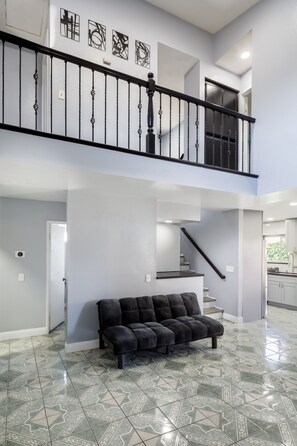 A spacious living area with a black sofa, a staircase, and a kitchen in the background.